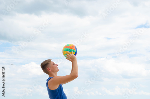 Portrait of a smiling volleyball player with colorfull ball at the cloudy sky background.