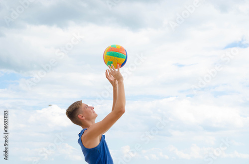 Portrait of a smiling volleyball player with colorfull ball at the cloudy sky background. © valerii kalantai