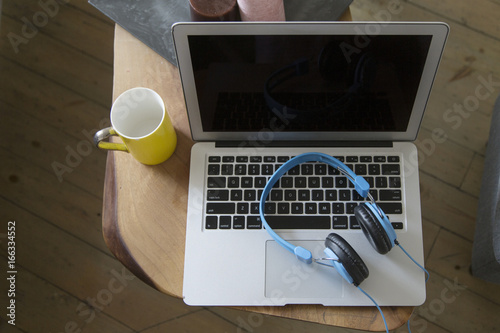 Headphones over laptop on wooden desk table with yellow cup photo