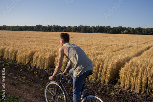 Young man ride fixed gear bike on the country road, fields and blue sky background 