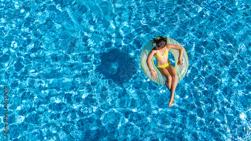 Aerial view of girl in swimming pool from above, kid swim on inflatable ring donut and has fun in water on family vacation

