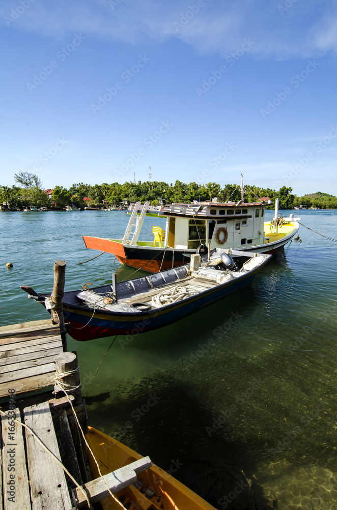 traditional malaysian fisherman boat moored, wooden jetty and blue sky background at sunny day