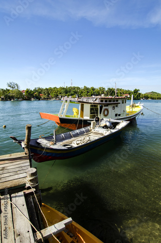 traditional malaysian fisherman boat moored  wooden jetty and blue sky background at sunny day