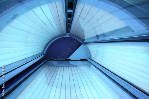 Solarium empty tanning bed in modern beauty salon, view from inside with closed lid and all light bulbs glowing on. Concept of sunbath, beauty lifestyle and healthcare photo
