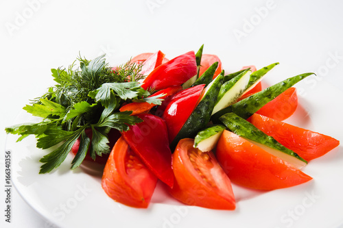 Vegetable salad - tomato, pepper, cucumber and greens on a white plate on a light background
