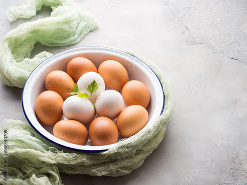 White and brown hen eggs in bowl on concrete gray background