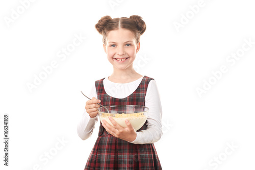 Portrait of cute girl in school uniform eating cereal with milk against white background