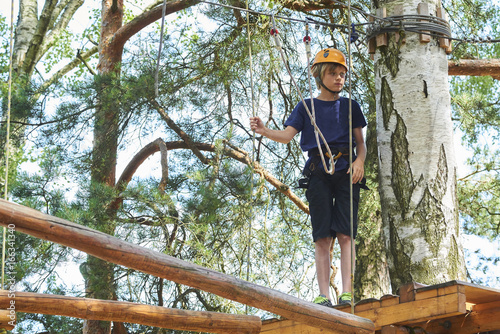 Child boy enjoys climbing in the ropes course adventure. Child engaged climbing high wire park. Active brave little boy enjoying climbing at treetop adventure park