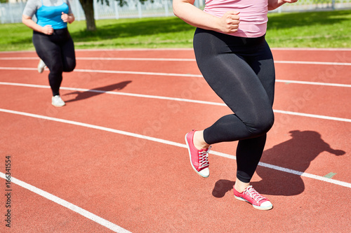 Low section of chubby female in activewear running on racetrack of stadium