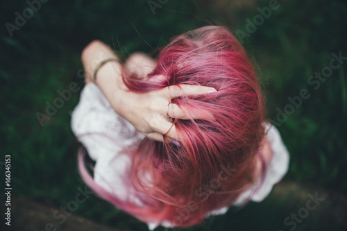 The beautiful girl with pink hair sits on the thrown ladder in an environment of a green grass