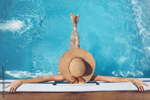 Back view of woman in straw hat relaxing in swimming pool on Tropical Resort. Exotic Paradise. Travel, Tourism and Vacations Concept.