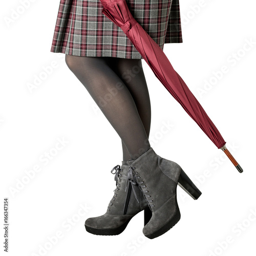 Female legs in gray pantyhose, a skirt in a cage and in gray suede boots on a heel with an umbrella on an isolated background.