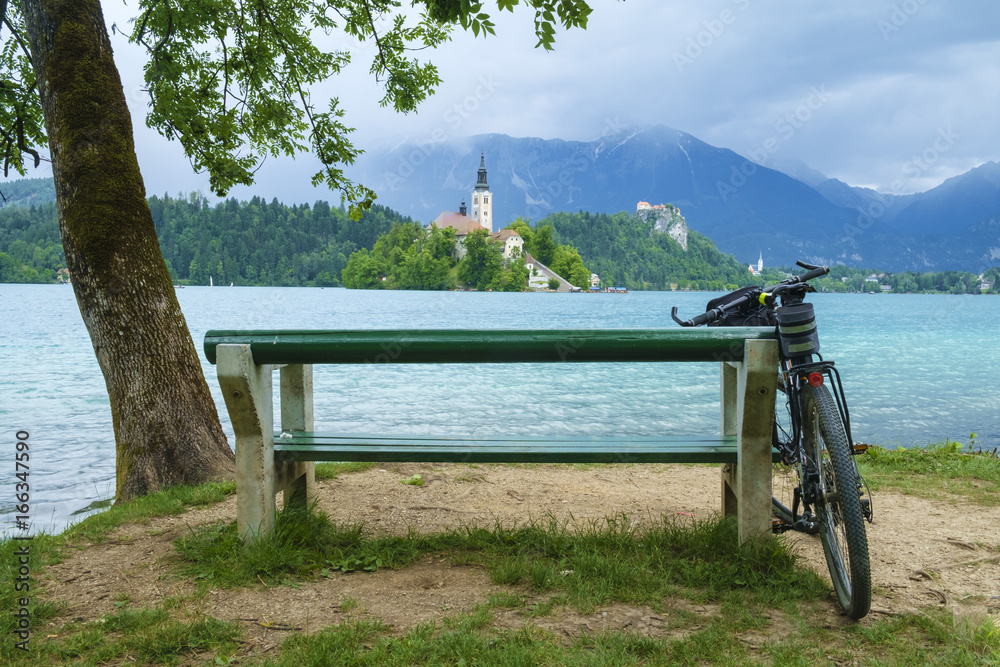 Fototapeta premium Bicycle leaning on the bench on the bank of Bled lake on a summer day.
