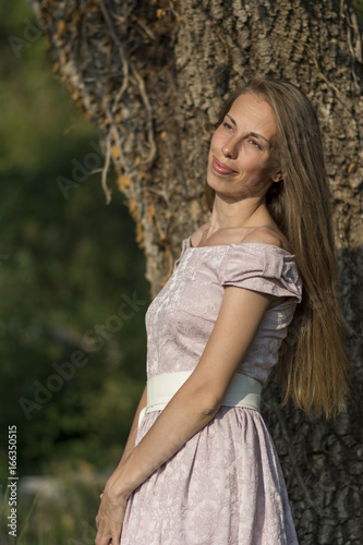 Beautiful woman portrait in a pink dress in front of a tree with ivy.
