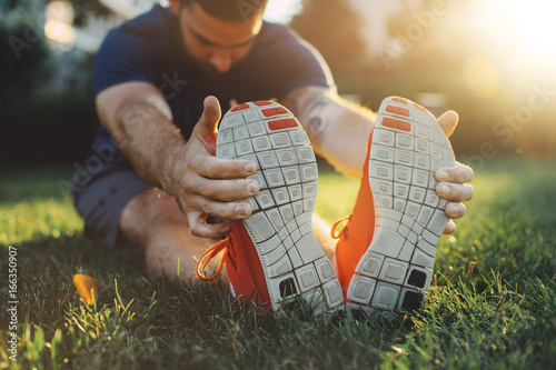 Attractive young man stretching in the park before running at the sunset focus on shoes photo