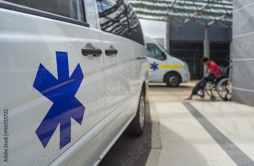 Ambulance avec étoile de vie devant un hopital et personne en  fauteuil roulante – Krankenwagen mit Star of life vor Krankenhaus und Person im Rollstuhl