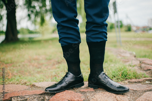 Unrecognizable man in wedding suit standing outdoor with socks put on trousers. Groom in black leather shoes standing on nature at stone. Freaky, foolish, absurd, odd clothes style. Funny marriage day