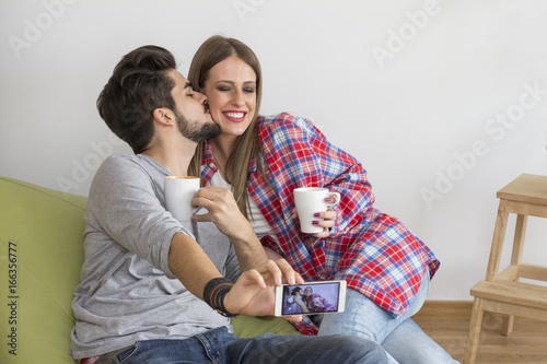 Young couple in new flat with coffee mugs in hand, he kiss her and she smile