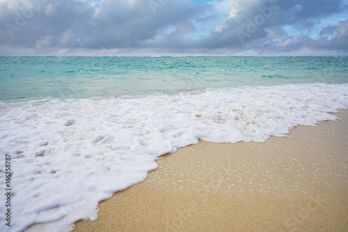 Background of sea sand beach which have movement wave of sea foam in tropical sunlight, Romantic peace and relax wide scene of a blue aqua menthe sea and summer season with copy space. 