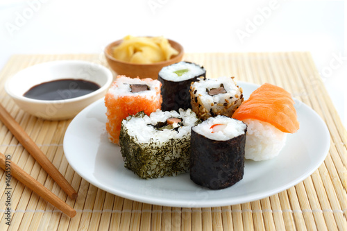Photo Selection of sushi on bamboo mat with chopsticks, soya sauce and pickled ginger