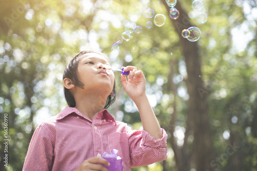 Cute Asian little girl Blowing soap bubble.Young Happy kid wear glasses and pink shirts in summer park.