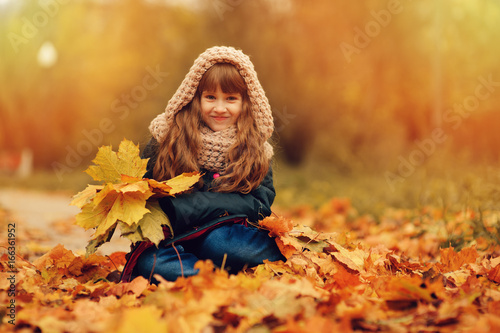 autumn outdoor portrait of beautiful happy child girl walking in park or forest in warm knitted scarf
