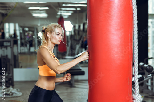 Athletic young woman training with punching bag at gym
