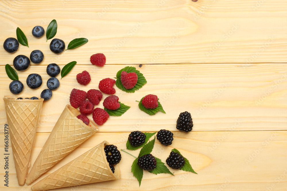 mix of blueberries, blackberries, raspberries in ice cream cone on light wooden table background. top view with copy space
