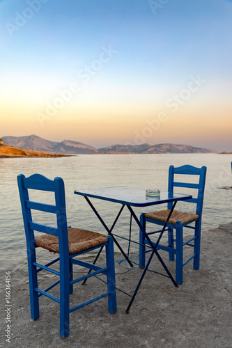 Klassisch  griechische St  hle und Tisch am Meer bei Sonnenuntergang  Kykladen  Griechenland