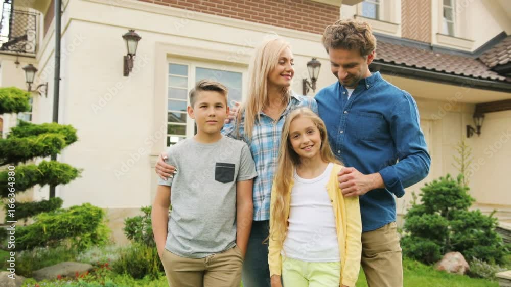 Happy caucasian family in front of new home, hugging and smiling on camera. Close up shot.