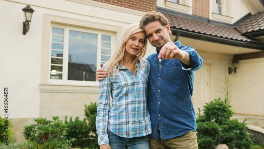 Portrait of attractive couple in love hugging and smiling on camera in front of new house. Portrait of attractive couple in love hugging and smiling on camera in front of new house.