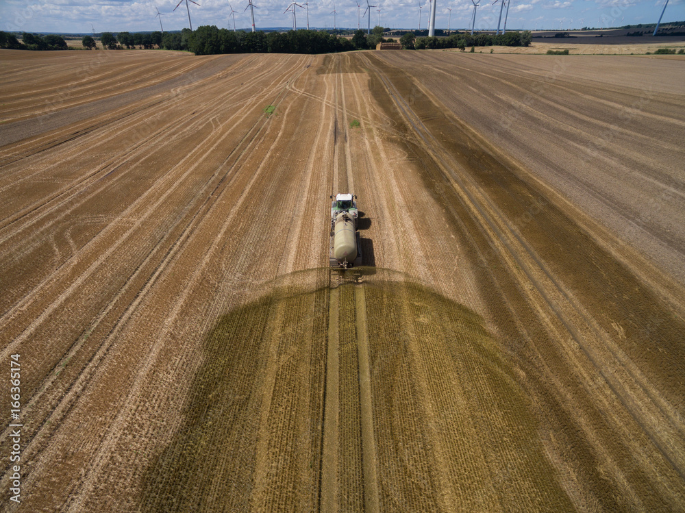 Naklejka premium aerial view of a tractor with a trailer fertilizes a freshly plowed agriculural field with manure in germany