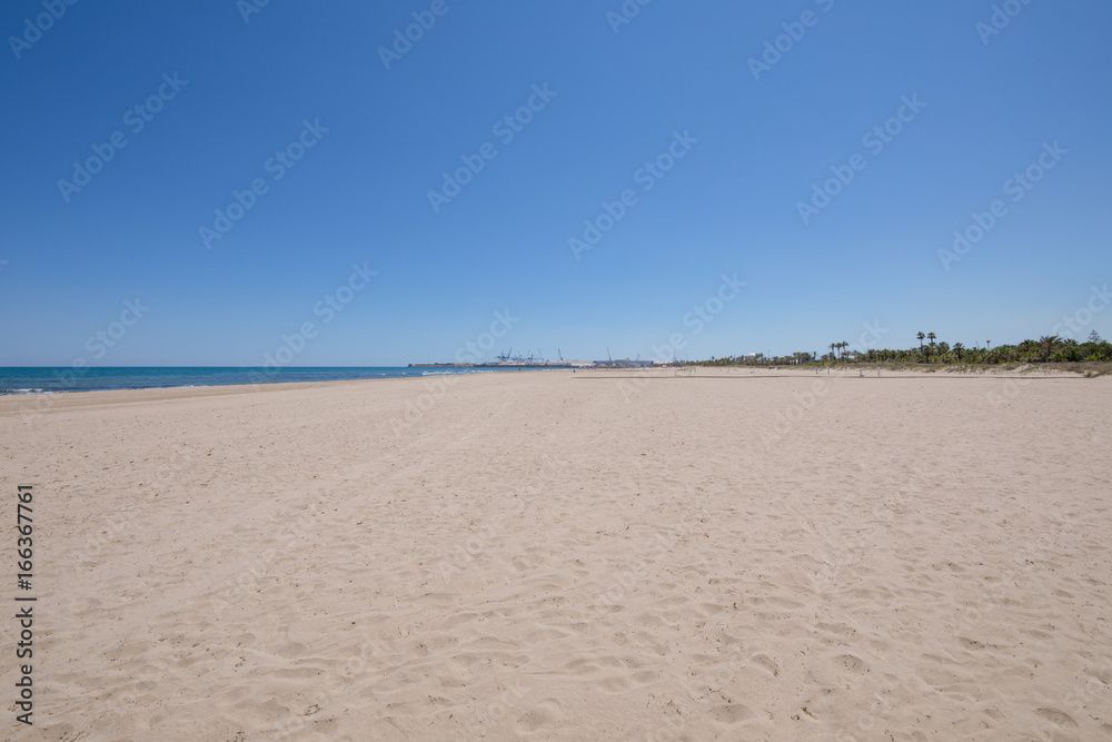 landscape beach in Grao of Castellon, named PIne or Pinar, in Valencia, Spain, Europe. Blue clear sky, Mediterranean Sea and harbour in the horizon
