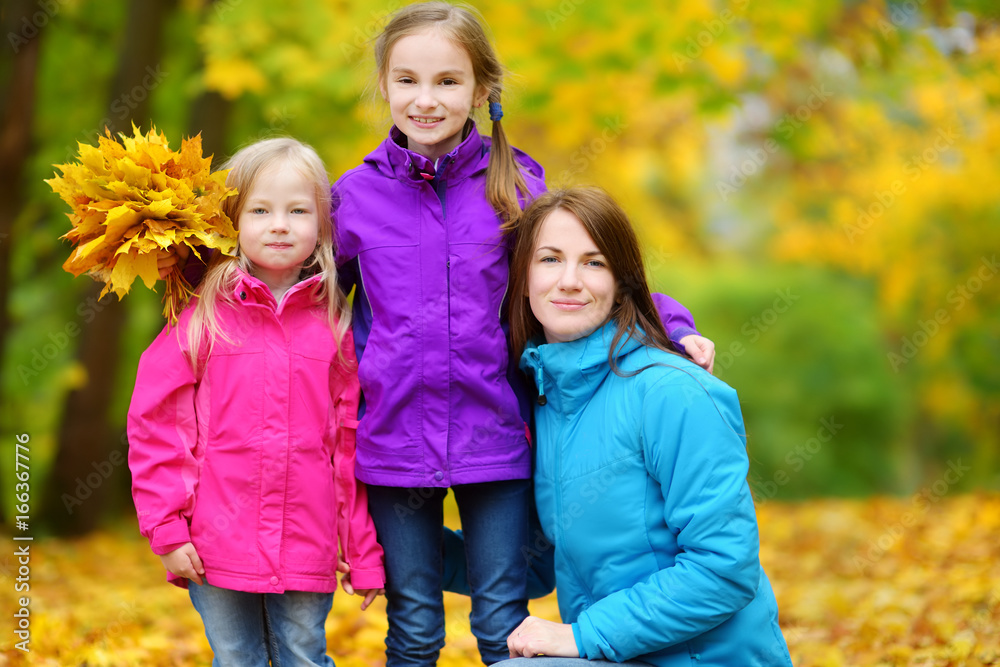 Cute little girls and their mother having fun on beautiful autumn day. Happy children playing in autumn park. Kids gathering yellow fall foliage.