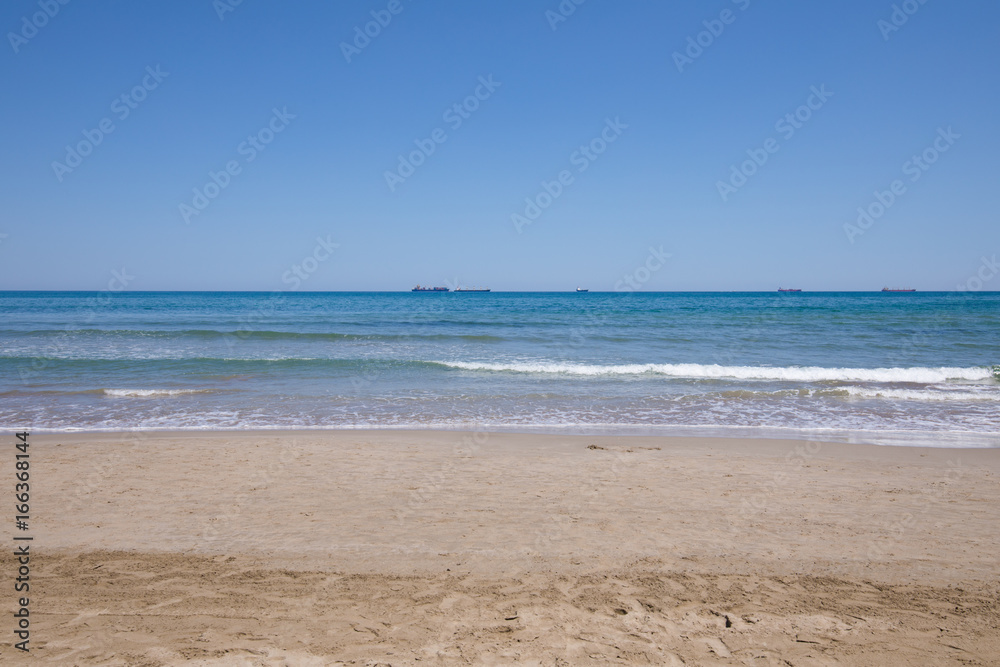 landscape of Mediterranean Sea from sand shore beach of Grao of Castellon, in Valencia, Spain, Europe. Blue clear sky, and great cargo boats sailing in the horizon

