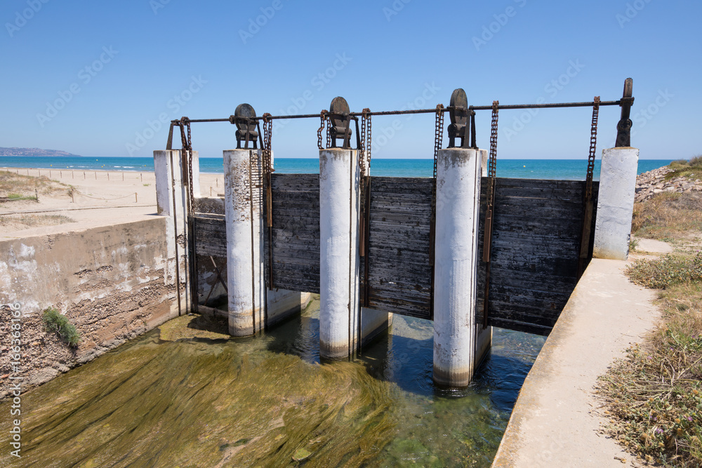 ancient sluices in waterway river towards Mediterranean Sea, next to Gurugu Beach in Castellon, Valencia, Spain, Europe. Blue clear sky
ancient sluices in waterway river towards Mediterranean Sea, next to Gurugu Beach in Castellon, Valencia, Spain, Europe. Blue clear sky