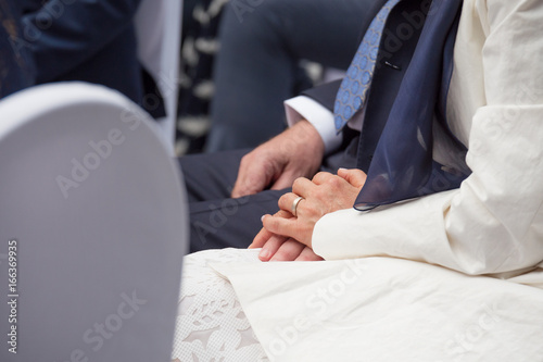 Bride holding grooms hands while seated during wedding ceremony