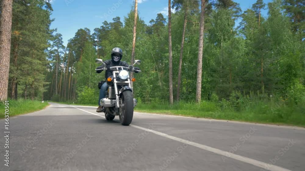 A skull face motorcyclist rides on a sunny road. A skull face motorcyclist rides on a sunny road.