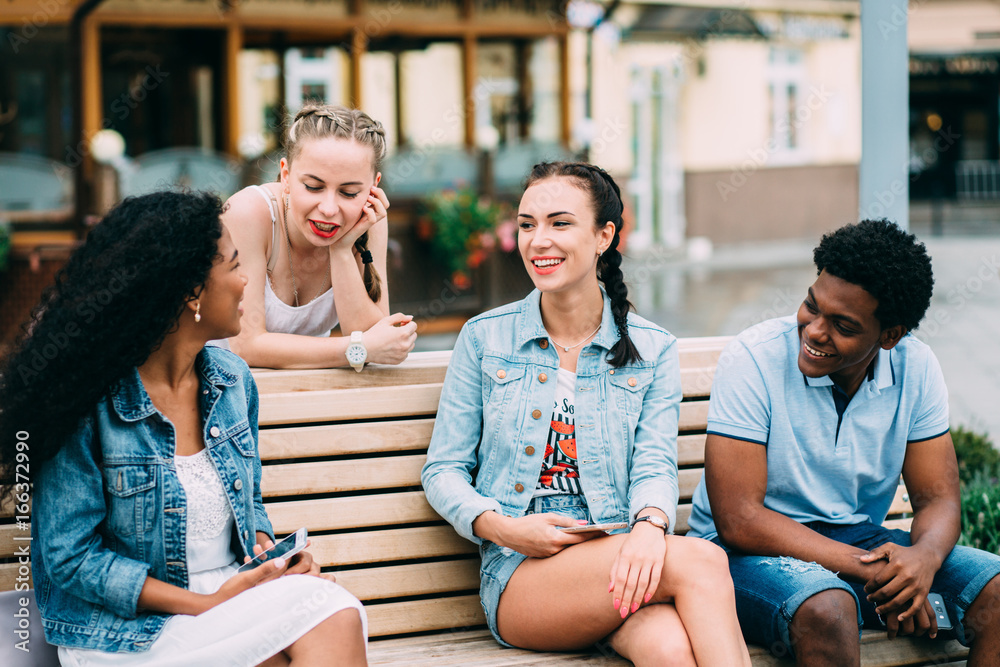 Series photo of group multiethnic hipster teenagers friends laughing and talking while sitting on the bench outdoor in ciity center.People, leisure, friendship, technology and communication concept