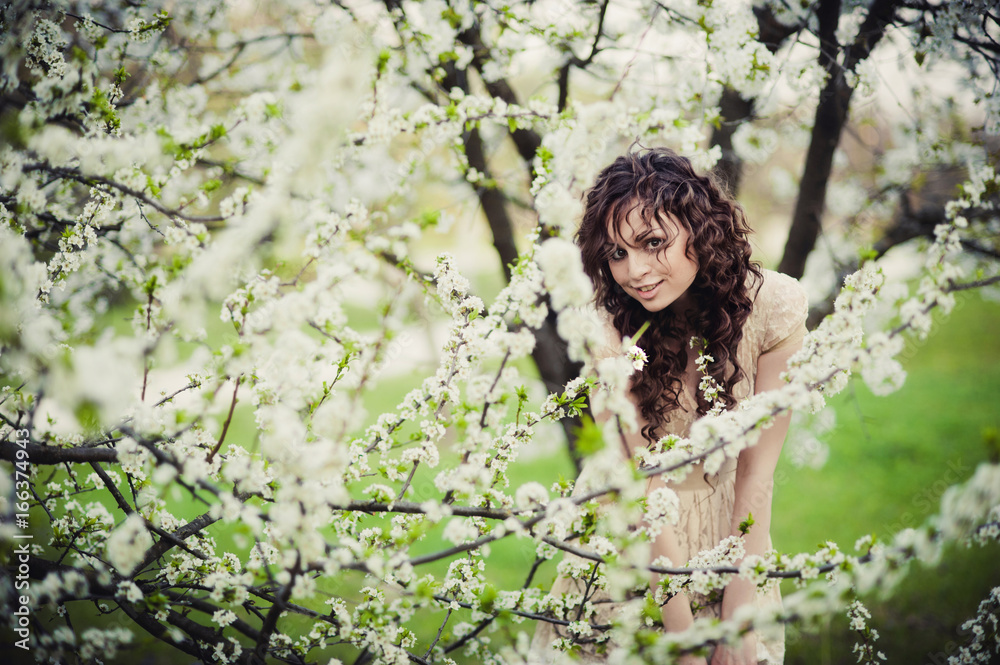 Curly brunette girl standing in blossoming trees Curly brunette girl standing in blossoming trees