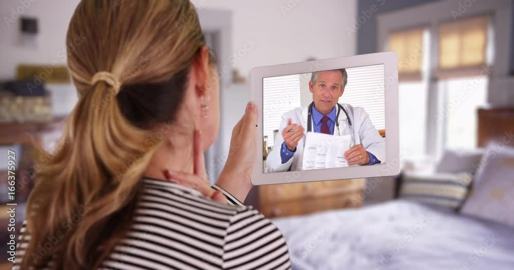 Woman having video chat with white male doctor using tablet inside bedroom