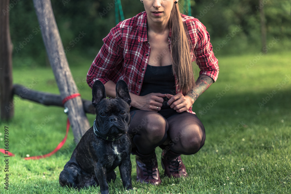 Young woman with tattoo sitting on grass with French Bulldog Young woman with tattoo sitting on grass with French Bulldog