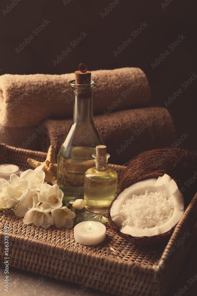 Fototapeta premium Spa oil in bottles, candle, coconuts and flowers on tray