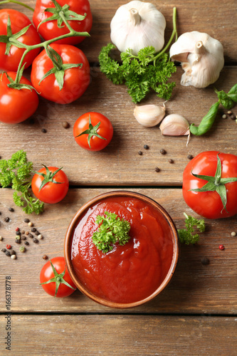 Bowl with sauce, tomatoes, greenery and spices on wooden table