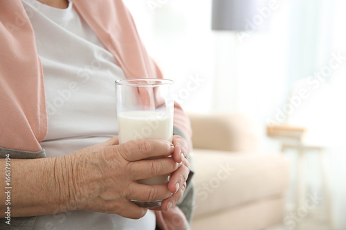 Old woman holding glass with fresh milk, closeup