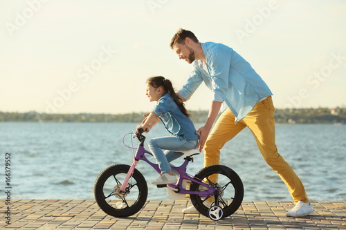 Young man teaching his daughter to ride bicycle outdoors near river