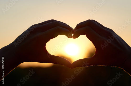 The silhouette of the heart of the hands in the center of its Sun. The concept of love and happiness