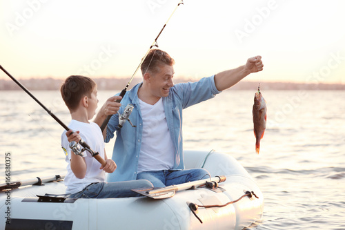 Canvas Print Dad and son fishing from inflatable boat on river