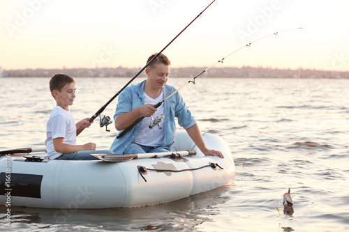 Dad and son fishing from inflatable boat on river