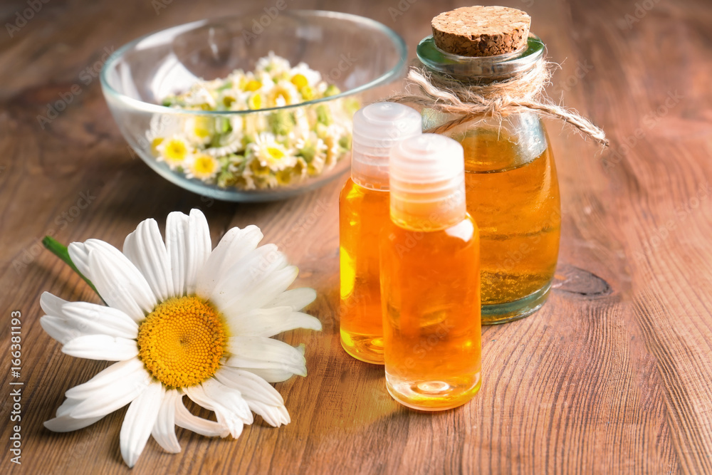 Bottles of essential oil and chamomile flowers on table Bottles of essential oil and chamomile flowers on table